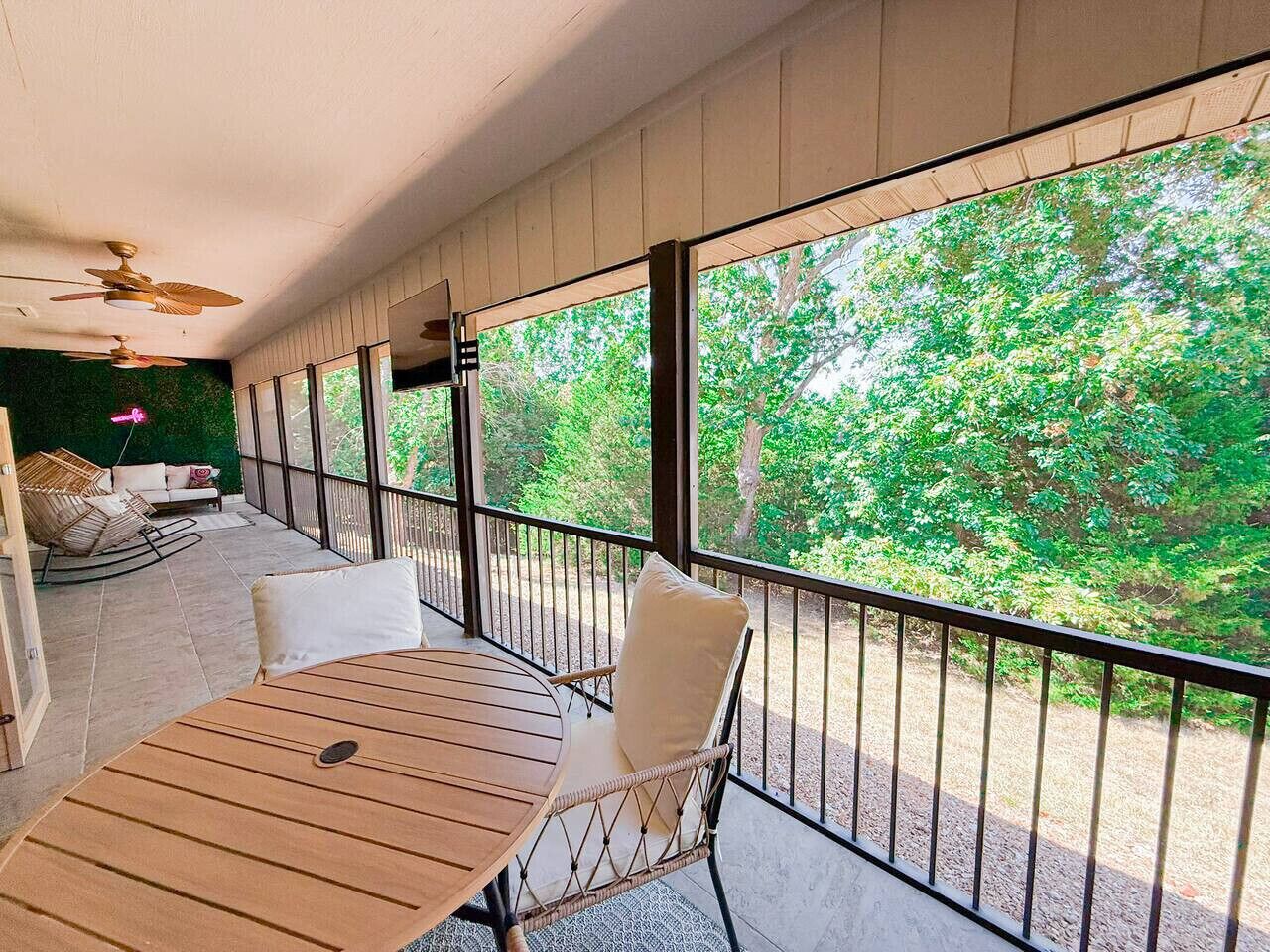 Een balkon met een houten tafel en stoelen, grote ramen met uitzicht op groen.