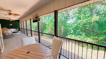 Een balkon met een houten tafel en stoelen, grote ramen met uitzicht op groen.