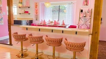 Een roze bar met vier comfortabele barstoelen en een toog.