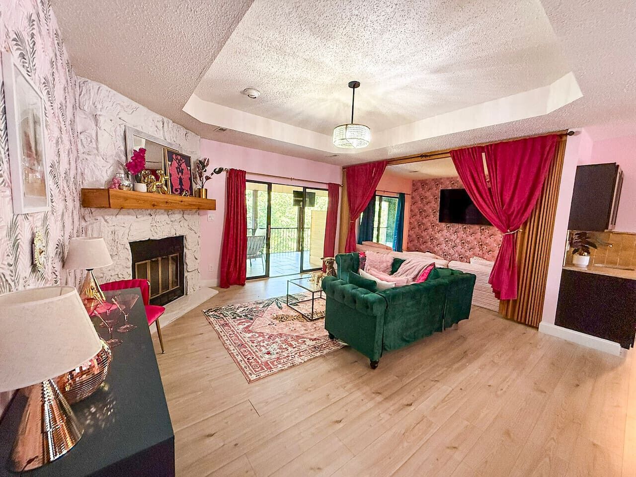 A living room with a fireplace, a green sofa, a red curtain, and a wooden floor.