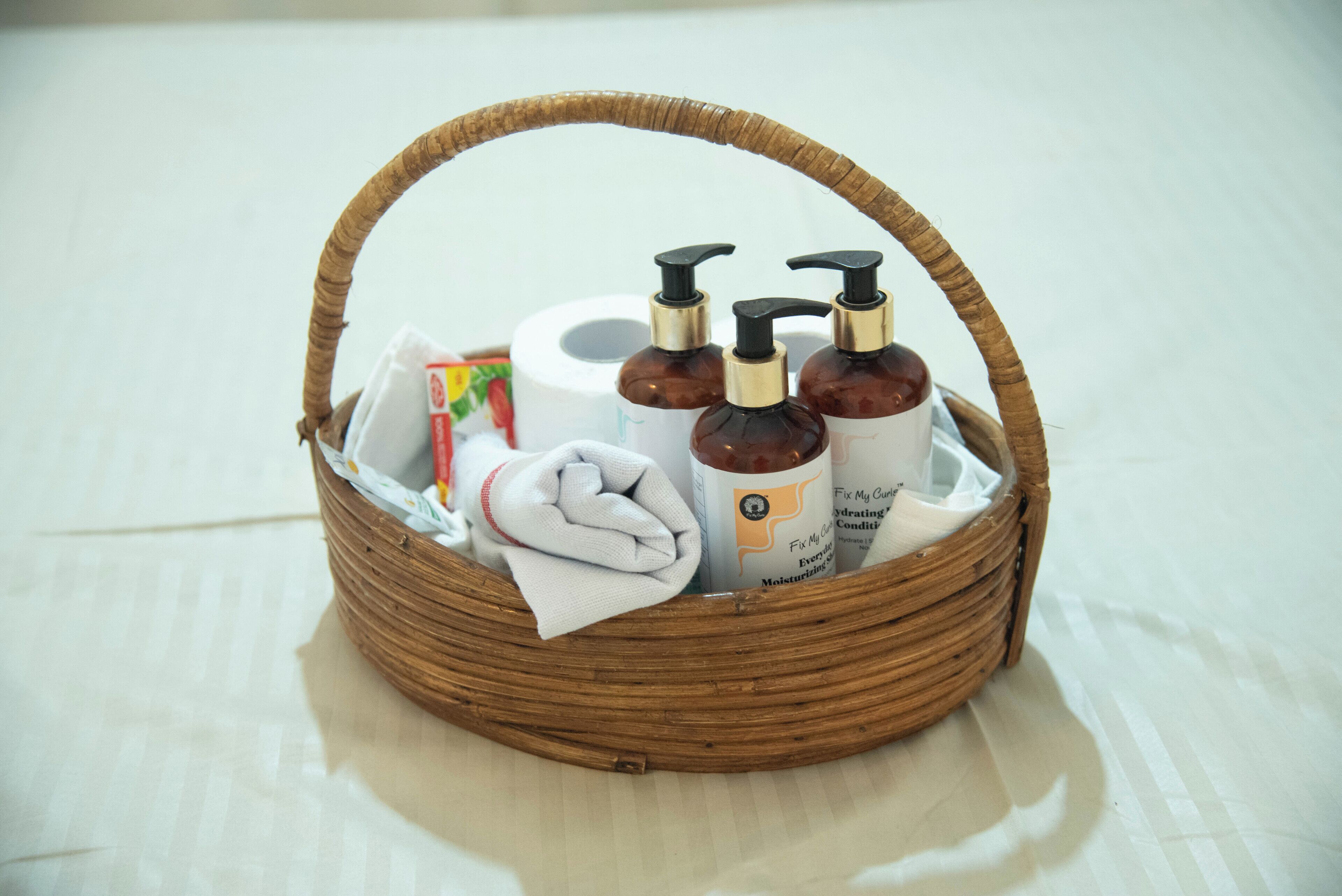 Cestino di vimini con articoli da bagno, fazzoletti e un asciugamano piegato.