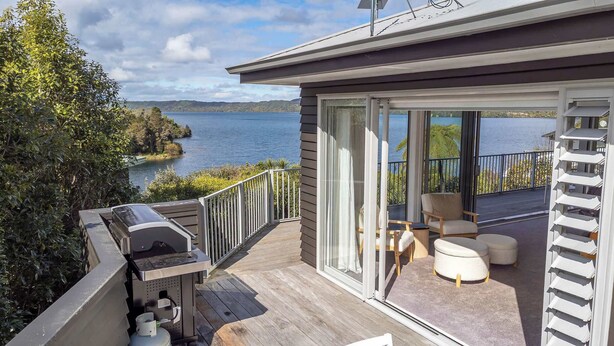 Una terraza con una parrilla, asientos exteriores y vista a un lago.