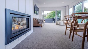 Una sala de estar moderna con chimenea, un sofá, una mesa de comedor con sillas y ventanas grandes.