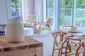 Une pièce chaleureuse avec une grande fenêtre, une table en bois avec des chaises et un vase blanc posé sur une surface en bois.