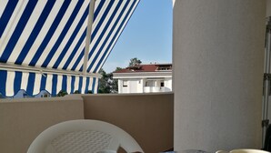 Uma varanda com toldo listrado, uma mesa com croissants, uma cafeteira e uma xícara.