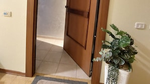 Um corredor com uma porta de madeira, um vaso pequeno com planta e um interruptor de luz na parede.