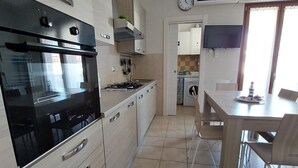 Cozinha moderna com forno embutido, fogão e armários. Há uma área de jantar com mesa e cadeiras.