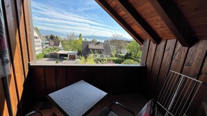 A small balcony with a table and chairs, wooden walls, and a view of houses and mountains.