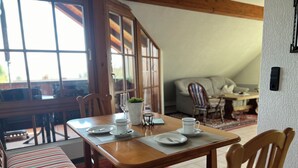 A dining area with a wooden table set for two, a bench, and a potted plant.