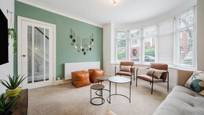 Una sala de estar con pared verde, puerta blanca, sofá de cuero marrón, sillón de cuero marrón, una mesita de centro redonda y una pequeña mesita auxiliar.