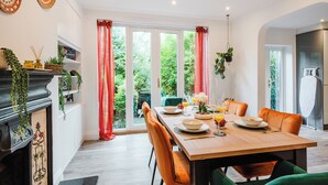 Un comedor con mesa de madera, sillas color naranja y vista a follaje a través de amplios ventanales.