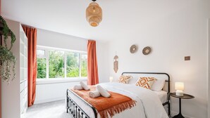 Un dormitorio con cama, mesita de noche con lámpara, ventana con cortinas y adornos en la pared.