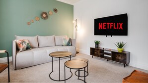 Una sala de estar con un sofá, dos mesas de centro, un televisor montado en la pared, un aparador y decoración mural.