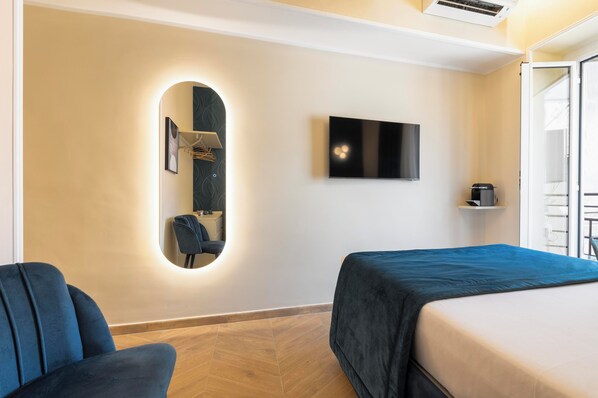 A hotel room with a bed, a chair, a TV, and a mirror with built-in lighting.