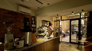 Interno di una caffetteria con bancone, macchine da caffè e zona salotto.