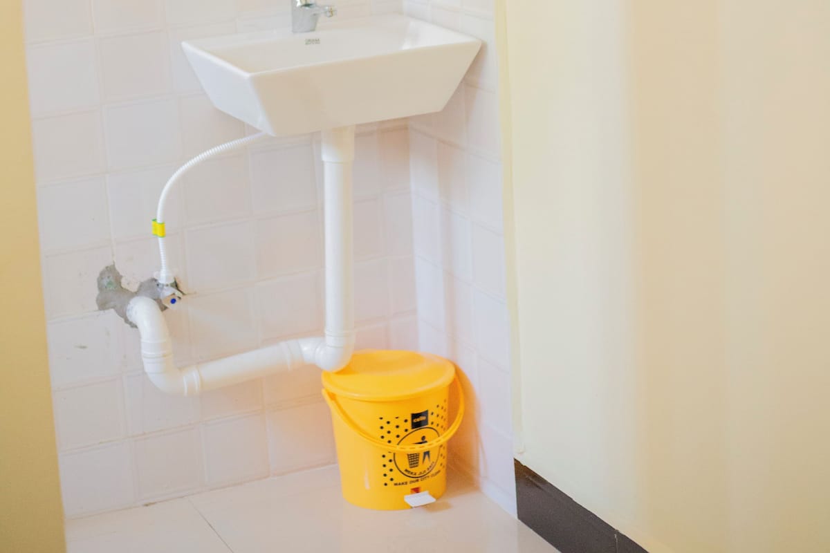 Casa de banho com lavatório branco, espelho e um balde amarelo.