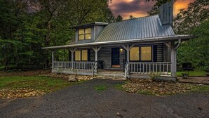 A two-story wooden house with a porch, large windows, and a metal roof.