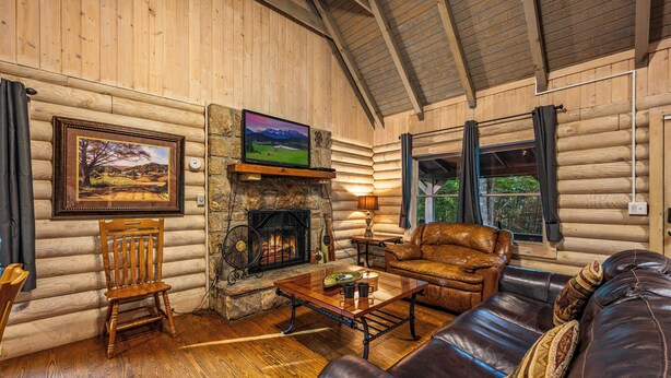 A log cabin interior with a fireplace, leather furniture, and a painting on the wall.