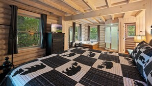 A log cabin bedroom with a large bed, a dresser, a vanity, and a window with curtains.