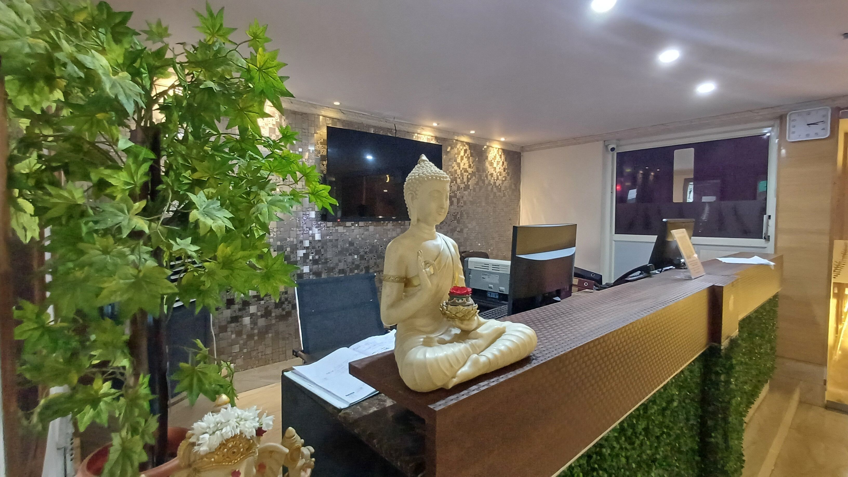 A reception desk with a Buddha statue, a computer, and a window with a view of the night sky.