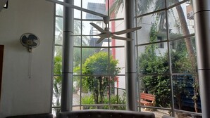 Una habitación con un ventanal grande, ventilador de techo y vistas a un patio con vegetación y una banca.