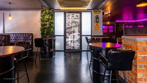 Interior de restaurante con barra, asientos acolchados y una pared verde con plantas.