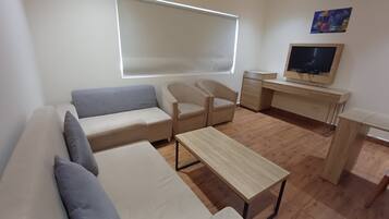 Een moderne woonkamer met een bank, twee fauteuils, een salontafel, een televisie en een bureau.