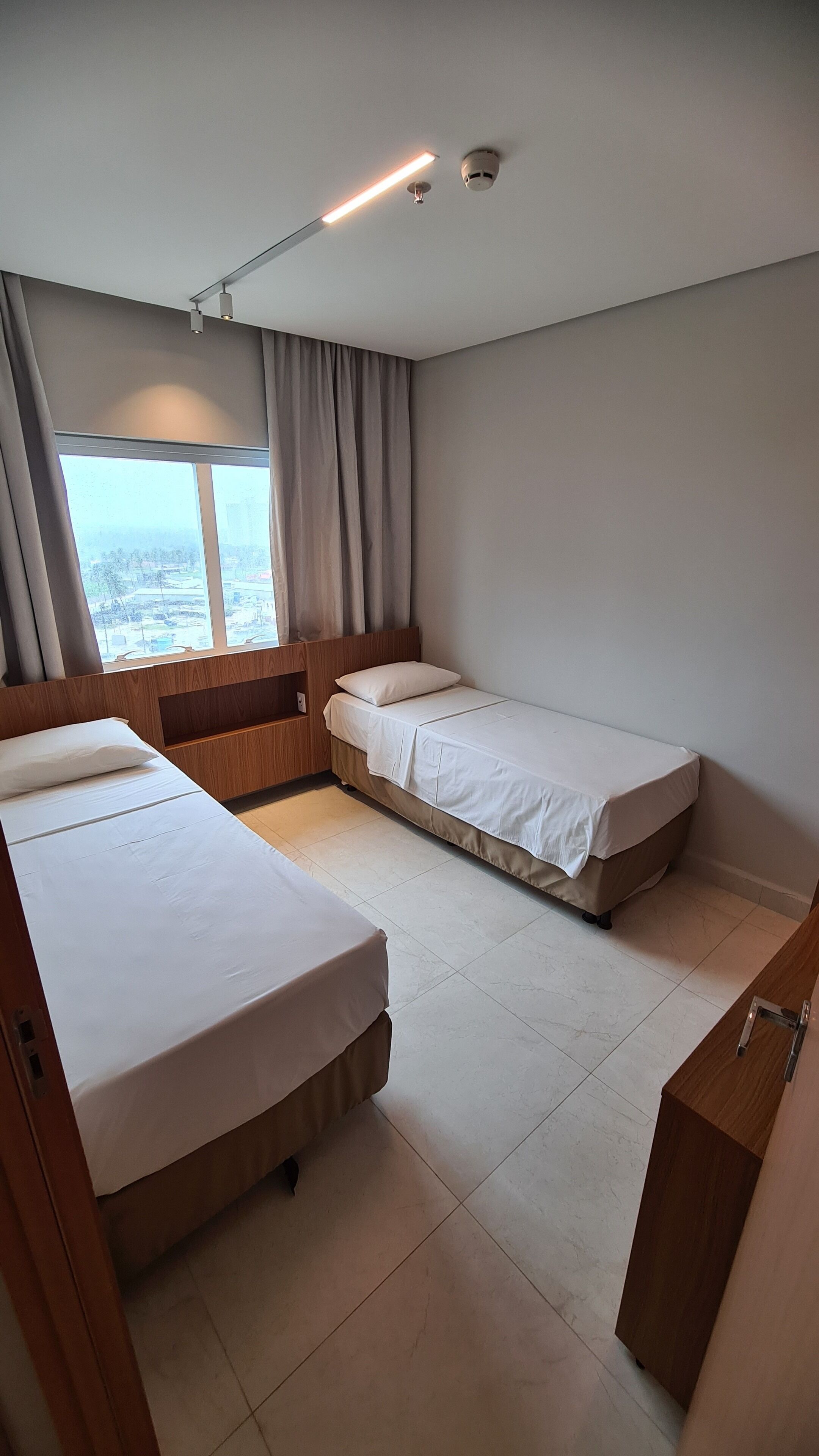 Camera da letto moderna con due letti, una testiera in legno, una finestra con tende e una lampada a soffitto.