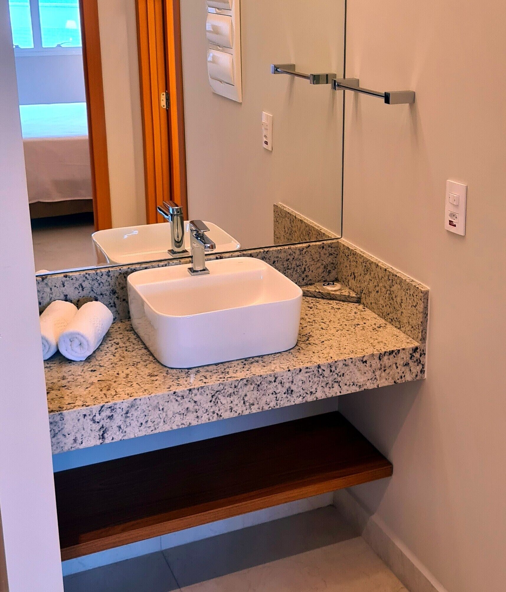 A bathroom with a white sink, granite countertop, and a mirror above it. There are towels on the countertop and a towel rack on the wall.