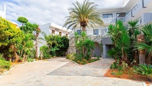 A courtyard with a stone pathway, palm trees, and a building with balconies. - HERMES HOTEL MALIA (Malia)