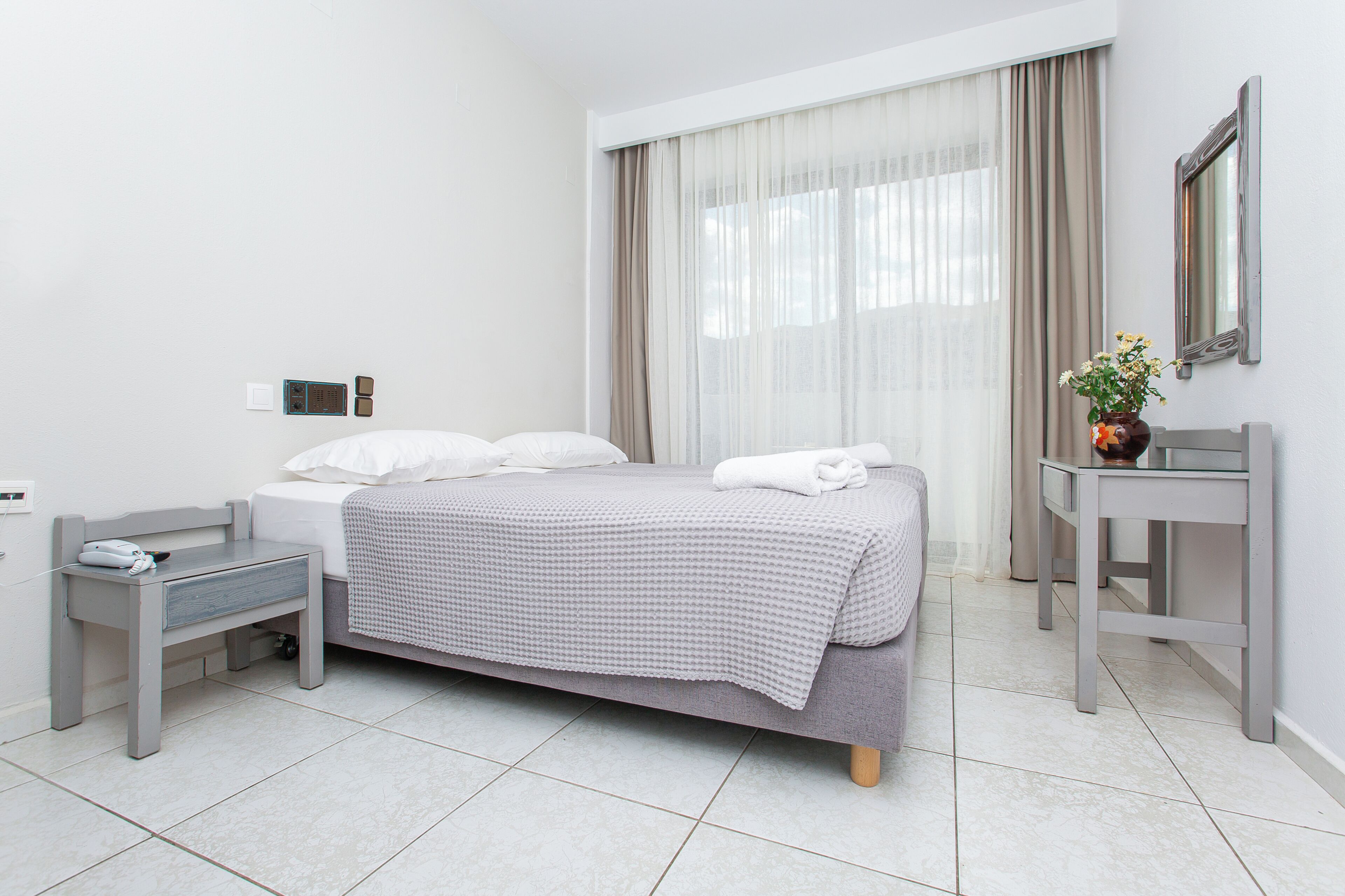A modern hotel room with a bed, bedside table, and a small desk with a chair.