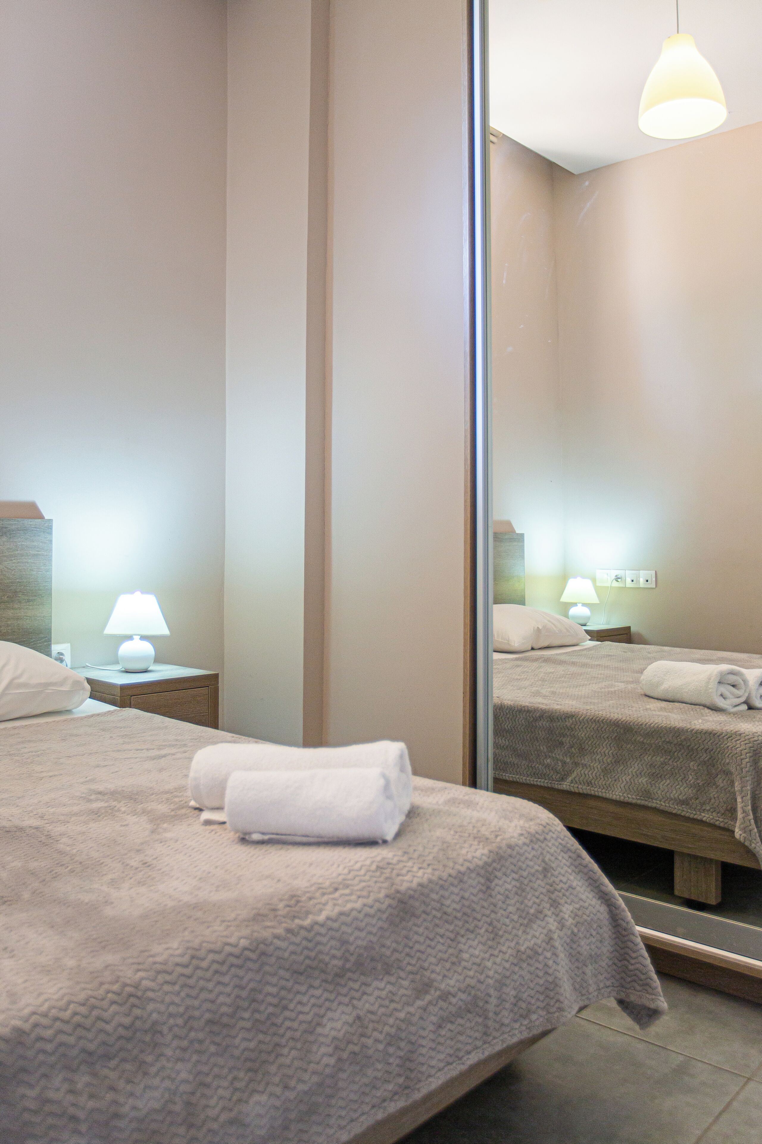 A hotel room with a bed, a nightstand with a lamp, a mirror, and a wall socket.