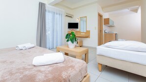 A hotel room with two beds, a TV, a mirror, a small table with a plant, and a window with curtains. - HERMES HOTEL MALIA (Malia)