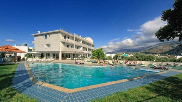 A swimming pool with lounge chairs and umbrellas, surrounded by a building with multiple floors and balconies. - HERMES HOTEL MALIA (Malia)