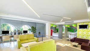 A modern lobby with seating areas, a reception desk, and a large window with a view of palm trees. - HERMES HOTEL MALIA (Malia)