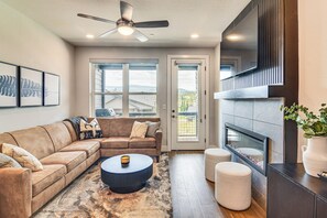 A modern living room with a sectional sofa, a round coffee table, a fireplace, and a large window offering a view of the outdoors. - Brand New Townhome w/ Hot Tub, 4 Mi to Winter Park (Fraser)