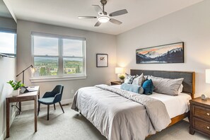 A bedroom with a bed, a desk, a chair, a nightstand, a lamp, a ceiling fan, a window, and a painting. - Brand New Townhome w/ Hot Tub, 4 Mi to Winter Park (Fraser)