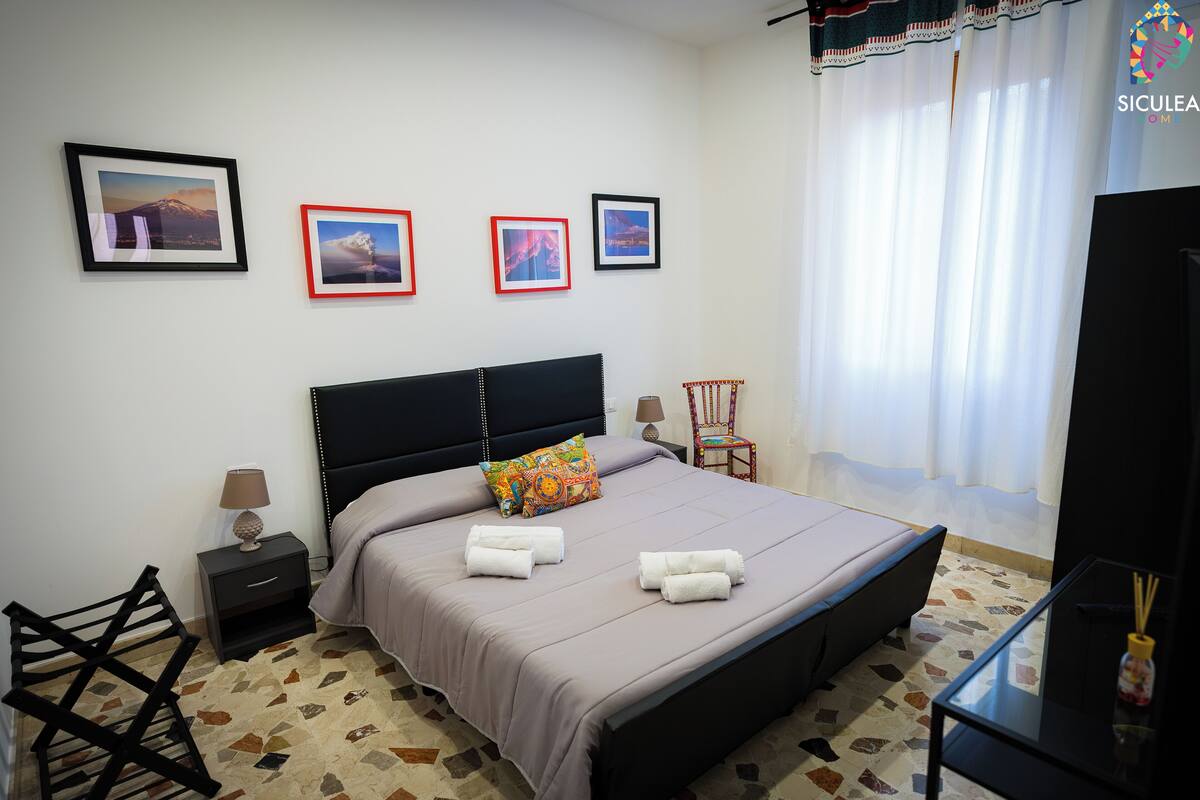 A neatly arranged bedroom with a bed, bedside tables, a chair, and a TV.