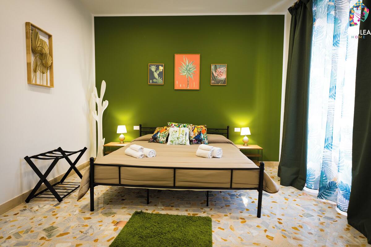 A bedroom with a bed, two bedside tables with lamps, a green wall, and artwork.
