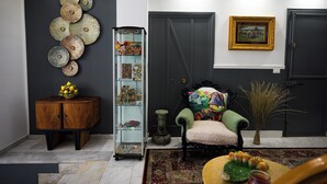 A living room with a dark wall, a glass display cabinet, a green armchair, a wooden cabinet, and a framed picture. - Siculea Home  (Adrano)
