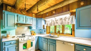 Une cuisine avec des meubles de couleur bleue, une cuisinière blanche et une fenêtre avec un rideau.