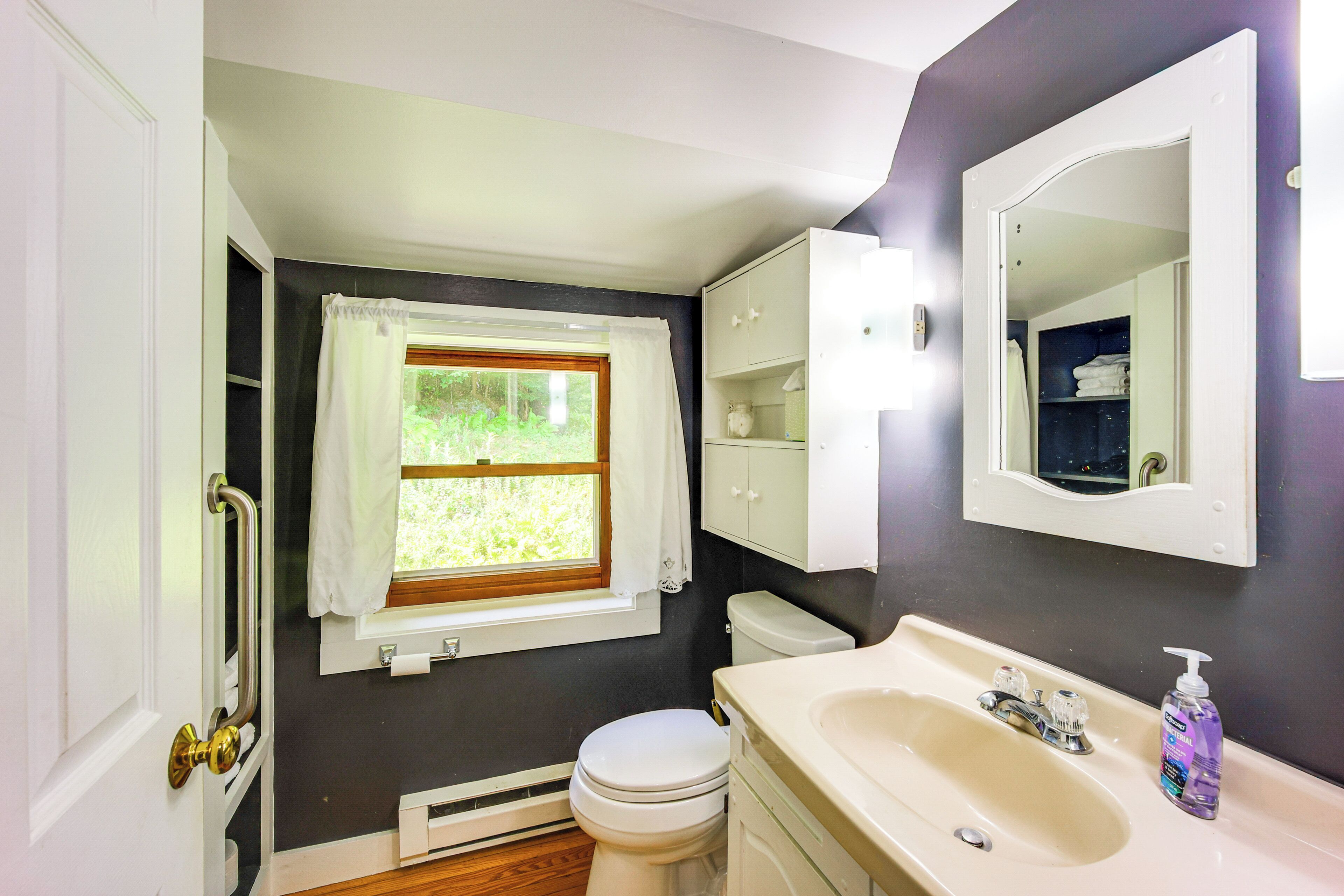 A bathroom with a window, white toilet, sink, and cabinet.