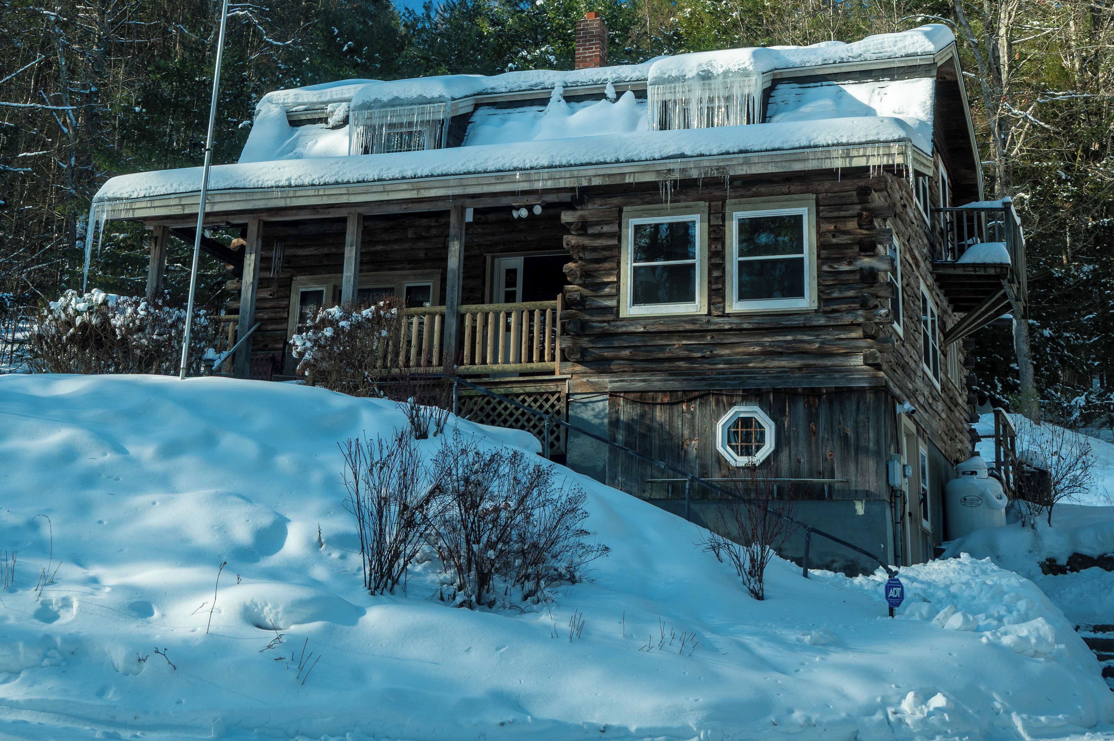 Une cabane en rondins dotée d’un porche et d’une terrasse supérieure couverte, entourée de neige et d’arbres.