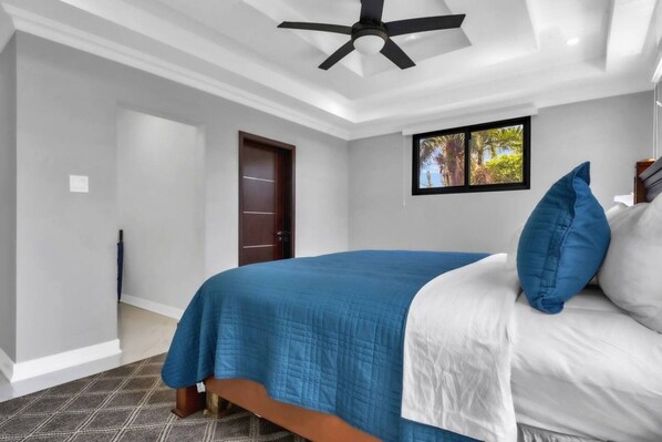 A bedroom with a bed, a ceiling fan, a door, and a window with a view.