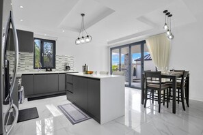 Una cocina moderna con una isla central, una zona de comedor con mesa y sillas, y un amplio ventanal corredero que da a un espacio exterior.