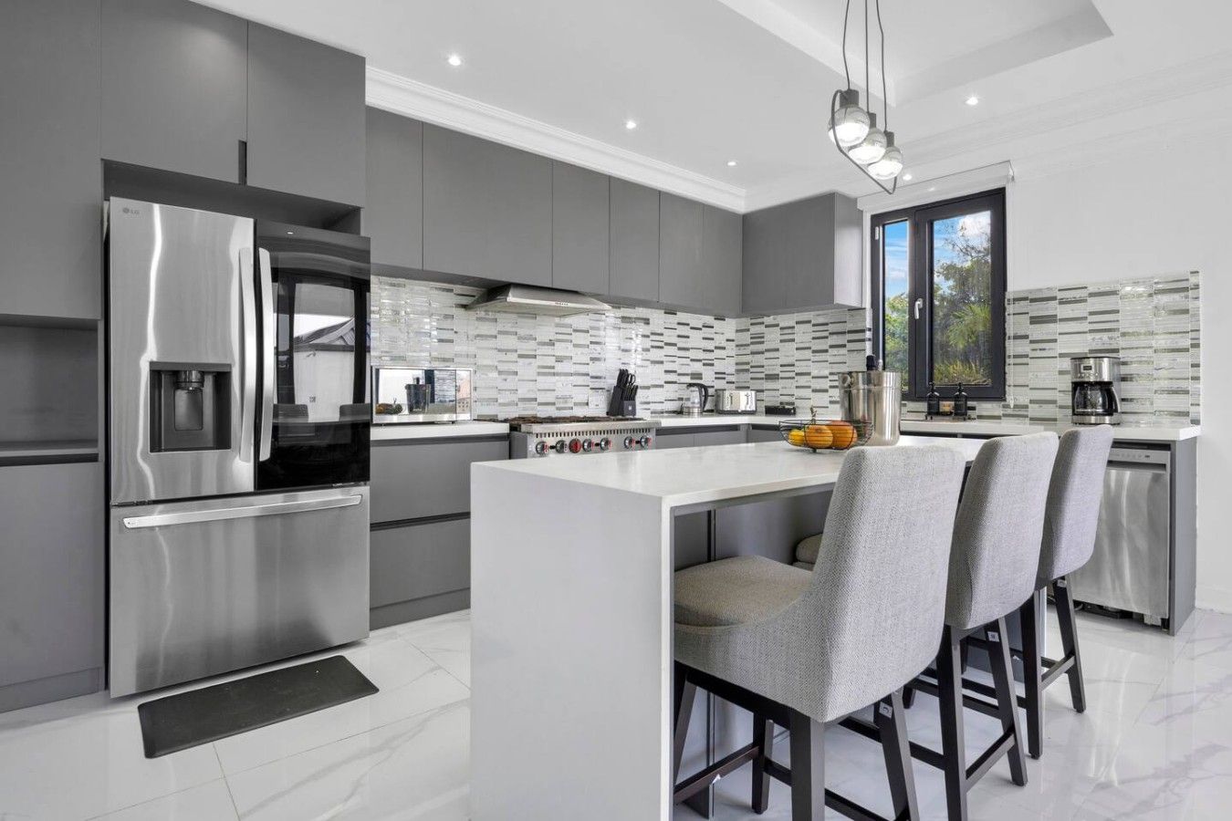 A modern kitchen with a stainless steel refrigerator, a built-in oven, and a large island with bar stools.