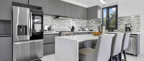 A modern kitchen with a stainless steel refrigerator, a built-in oven, and a large island with bar stools.