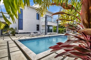 A modern pool area with a rectangular pool, lounge chairs, and a building with large windows.