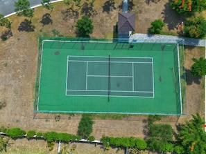An aerial view of a tennis court with surrounding greenery and a small building.