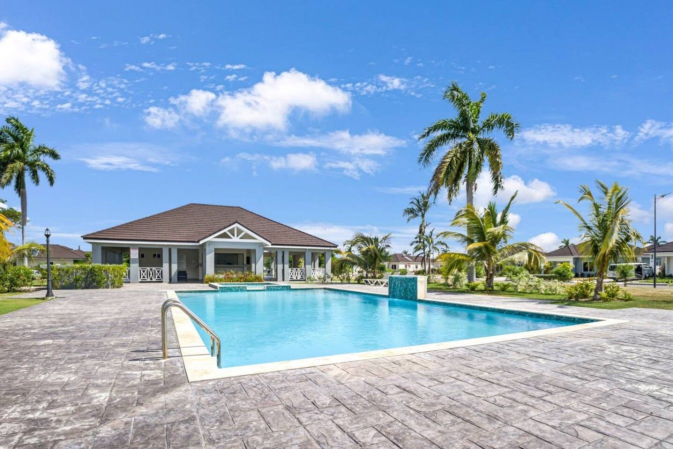 A swimming pool with a covered area, surrounded by palm trees and a clear sky.
